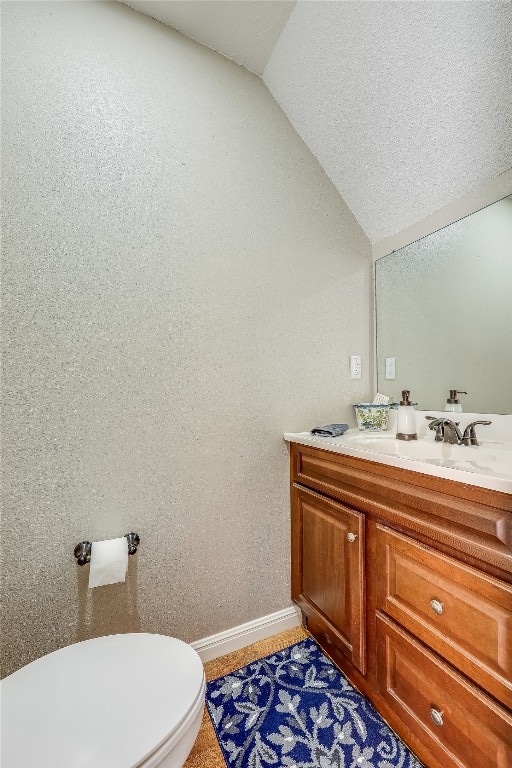 bathroom with lofted ceiling, vanity, toilet, and a textured ceiling