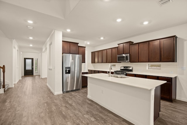 kitchen with dark brown cabinetry, a center island with sink, hardwood / wood-style floors, and appliances with stainless steel finishes