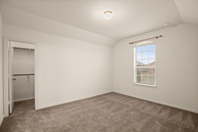 unfurnished bedroom with a closet, vaulted ceiling, a walk in closet, and carpet flooring