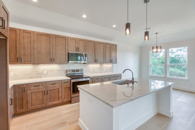 kitchen with light stone counters, stainless steel appliances, sink, decorative light fixtures, and a center island with sink