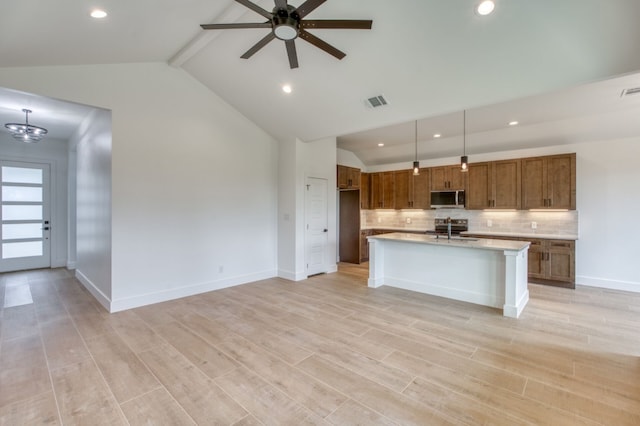 kitchen featuring backsplash, stainless steel appliances, a center island with sink, beamed ceiling, and hanging light fixtures