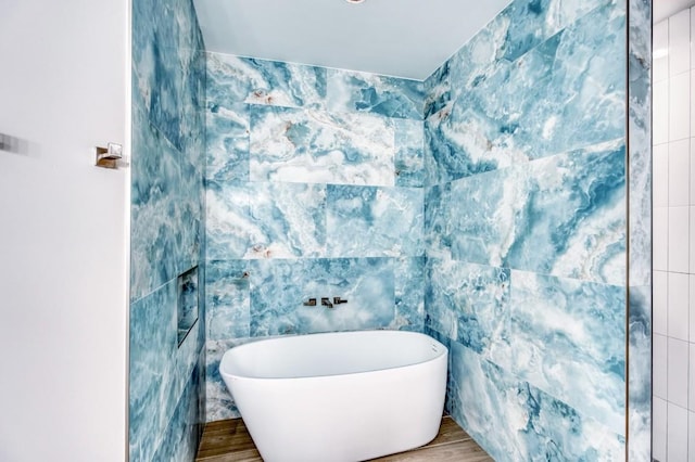 bathroom featuring a tub to relax in, hardwood / wood-style floors, and tile walls