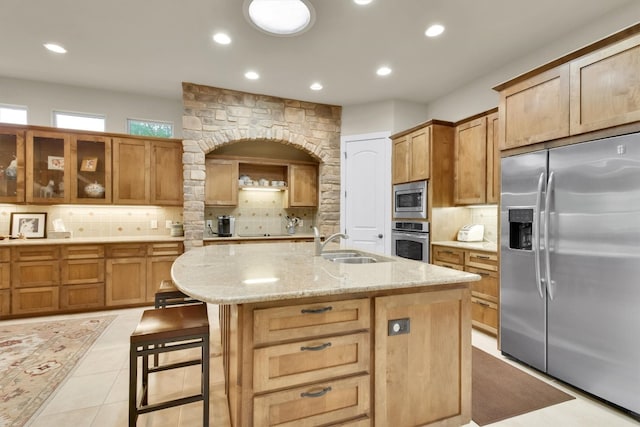 kitchen featuring light tile flooring, backsplash, sink, a kitchen island with sink, and appliances with stainless steel finishes