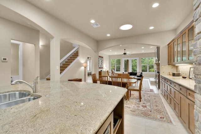 kitchen featuring ceiling fan, tasteful backsplash, light stone countertops, sink, and light tile floors