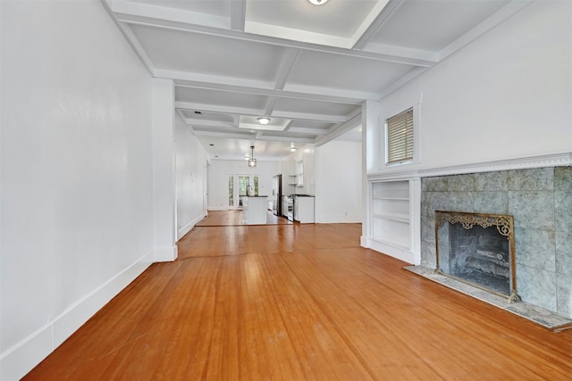 unfurnished living room featuring a tiled fireplace, coffered ceiling, wood-type flooring, and a wealth of natural light