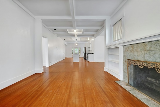 unfurnished living room featuring a fireplace, light wood-type flooring, sink, coffered ceiling, and beam ceiling