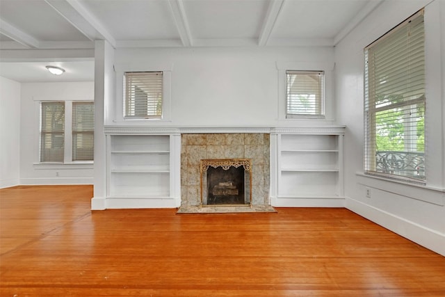 unfurnished living room featuring beamed ceiling, hardwood / wood-style floors, built in shelves, and a tile fireplace