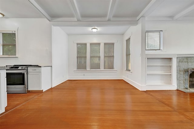 unfurnished living room featuring a tiled fireplace, built in shelves, beam ceiling, and light hardwood / wood-style floors