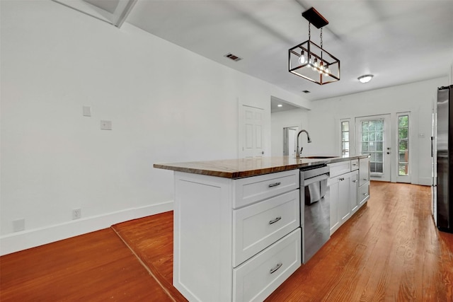 kitchen featuring white cabinetry, hanging light fixtures, appliances with stainless steel finishes, a center island with sink, and light hardwood / wood-style floors