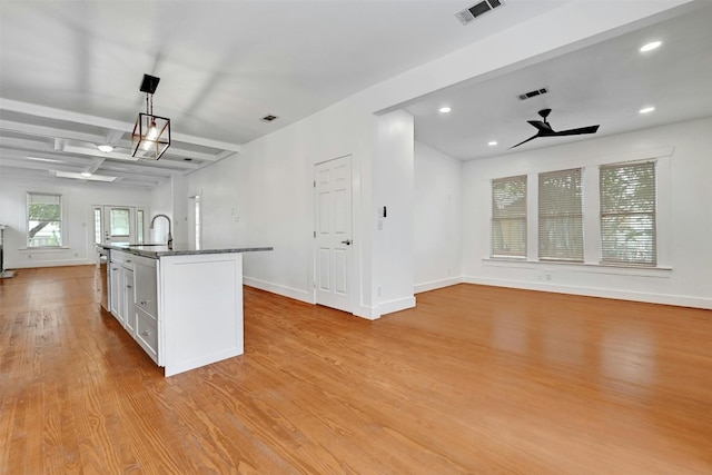 kitchen featuring white cabinets, hanging light fixtures, light hardwood / wood-style floors, an island with sink, and ceiling fan