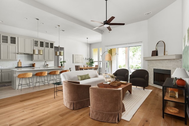 living area with ceiling fan, light wood-style flooring, a high ceiling, visible vents, and a brick fireplace