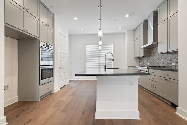 kitchen with dark countertops, wall chimney range hood, a sink, and gray cabinetry