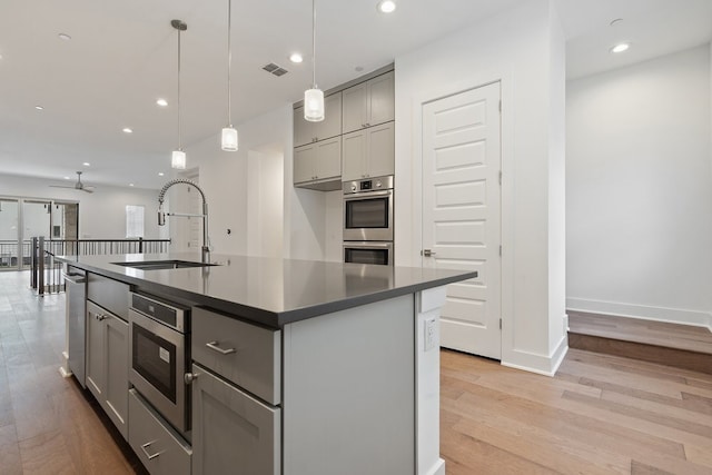 kitchen with dark countertops, visible vents, gray cabinetry, a sink, and an island with sink