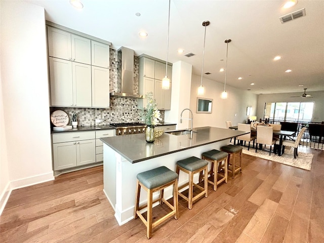 kitchen with dark countertops, visible vents, hanging light fixtures, a sink, and wall chimney exhaust hood