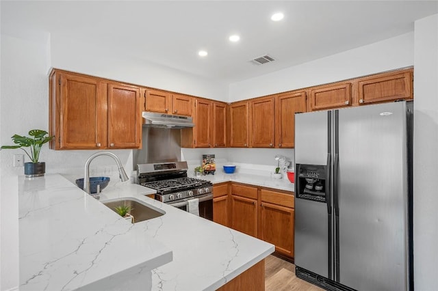 kitchen with sink, appliances with stainless steel finishes, light stone counters, light hardwood / wood-style floors, and kitchen peninsula