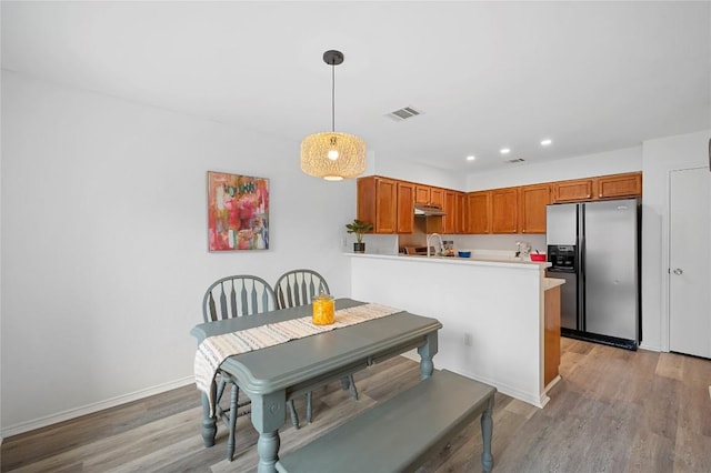 kitchen featuring pendant lighting, light hardwood / wood-style floors, sink, stainless steel fridge with ice dispenser, and kitchen peninsula