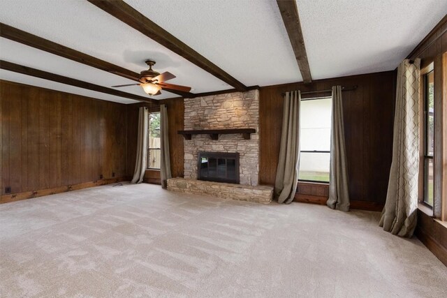 unfurnished living room with a fireplace, beam ceiling, ceiling fan, and light colored carpet