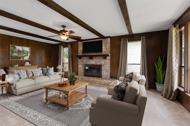 living room with beam ceiling, carpet, a fireplace, wooden walls, and ceiling fan