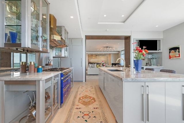 kitchen with a large island with sink, light hardwood / wood-style floors, light stone countertops, and stainless steel range