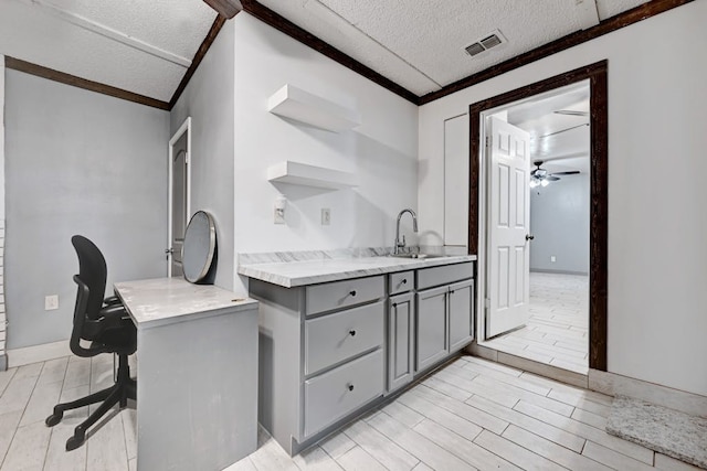 interior space with ceiling fan, a textured ceiling, sink, light wood-type flooring, and ornamental molding