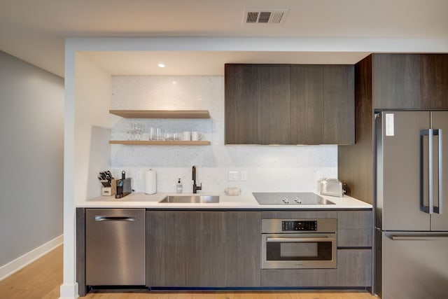 kitchen with dark brown cabinets, tasteful backsplash, light wood-type flooring, stainless steel appliances, and sink