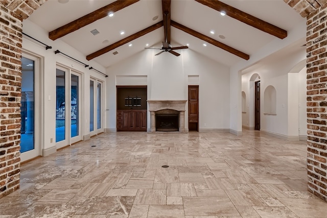 unfurnished living room featuring high vaulted ceiling, beamed ceiling, a large fireplace, ceiling fan, and french doors