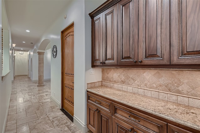 bar featuring light stone counters, ornate columns, and decorative backsplash