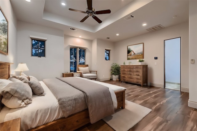 bedroom with multiple windows, a raised ceiling, dark hardwood / wood-style flooring, and ceiling fan