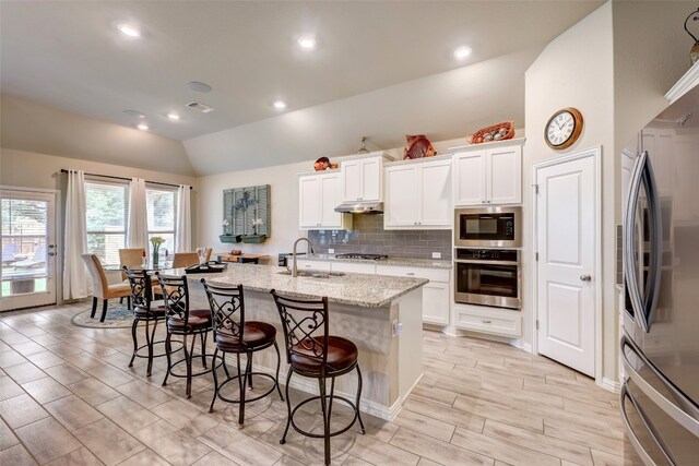 kitchen with appliances with stainless steel finishes, vaulted ceiling, sink, white cabinets, and an island with sink