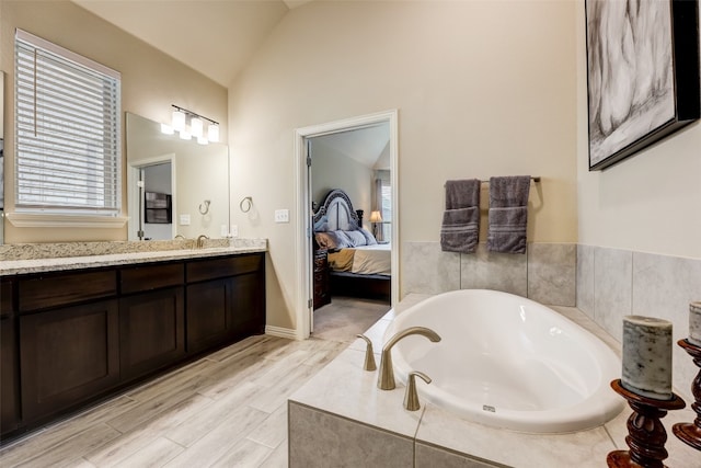 bathroom featuring vanity, hardwood / wood-style flooring, vaulted ceiling, and a relaxing tiled tub