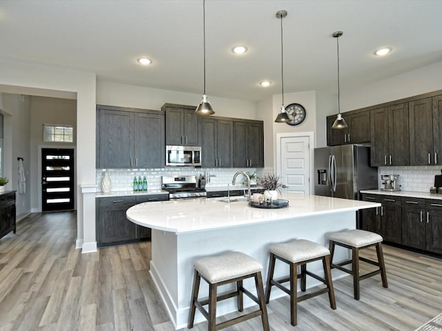 kitchen with stainless steel appliances, light hardwood / wood-style flooring, tasteful backsplash, and pendant lighting