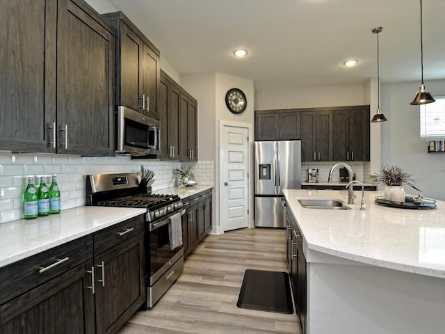 kitchen with light stone countertops, light wood-type flooring, stainless steel appliances, sink, and tasteful backsplash