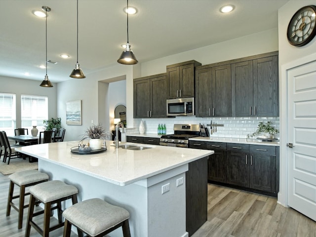 kitchen with decorative light fixtures, light hardwood / wood-style flooring, stainless steel appliances, backsplash, and sink