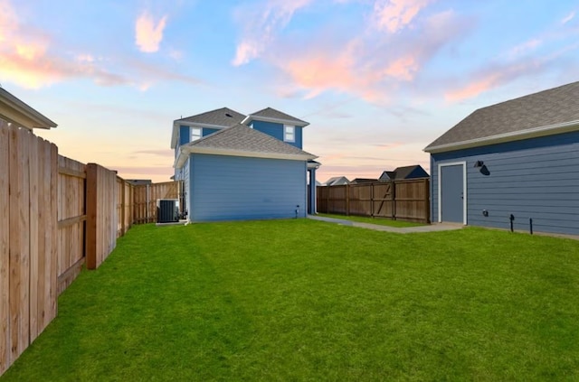 back house at dusk featuring a lawn and central AC