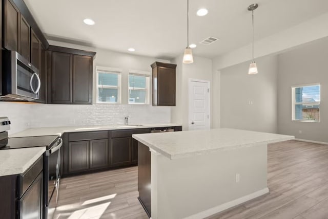 kitchen featuring appliances with stainless steel finishes, light wood-type flooring, decorative light fixtures, and a center island