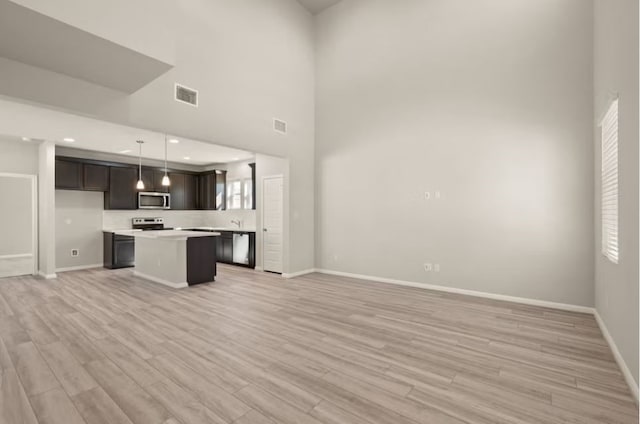 kitchen with appliances with stainless steel finishes, light wood-type flooring, decorative light fixtures, a high ceiling, and a kitchen island