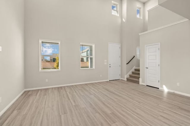 unfurnished living room with a towering ceiling and light wood-type flooring