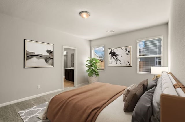 bedroom with ensuite bathroom and light colored carpet