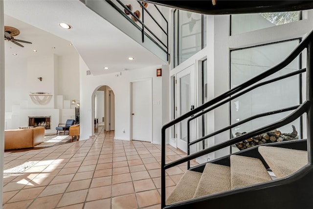 foyer entrance with light tile patterned floors, arched walkways, a fireplace with raised hearth, stairs, and a high ceiling