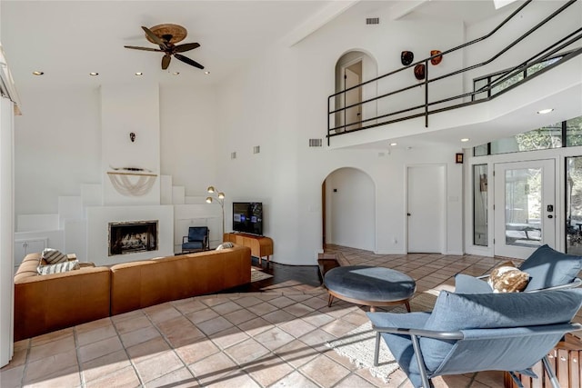 living area featuring arched walkways, a fireplace, light tile patterned floors, visible vents, and a towering ceiling