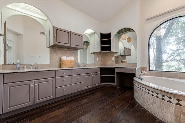 bathroom featuring a garden tub, a sink, wood finished floors, double vanity, and tasteful backsplash