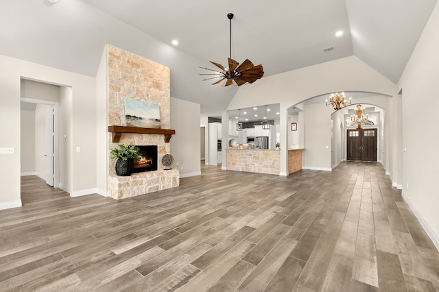 unfurnished living room featuring a fireplace, light wood-type flooring, ceiling fan with notable chandelier, and high vaulted ceiling