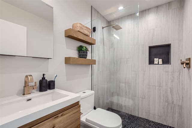 bathroom featuring a tile shower, vanity, and toilet