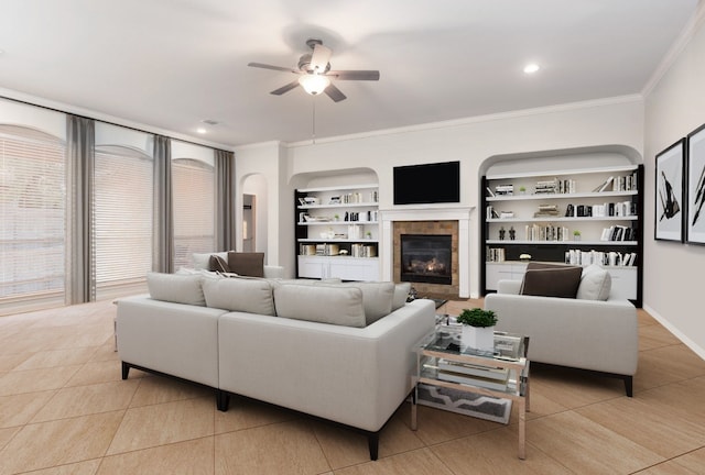 living room featuring ceiling fan, built in features, crown molding, a fireplace, and light tile patterned floors