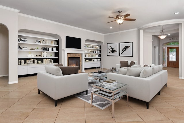 living room with built in shelves, ceiling fan, crown molding, and light tile patterned flooring