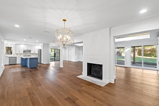 unfurnished living room with a brick fireplace, hardwood / wood-style flooring, and an inviting chandelier