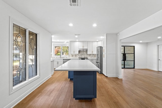 kitchen with light hardwood / wood-style floors, a kitchen island, white cabinetry, and a breakfast bar area