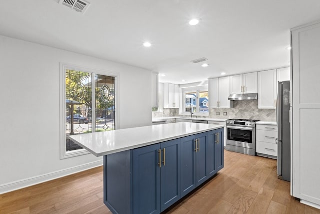 kitchen featuring white cabinets, blue cabinets, decorative backsplash, light wood-type flooring, and stainless steel appliances