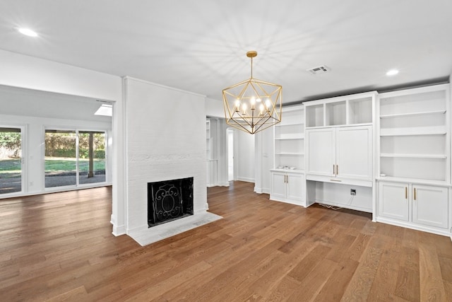 unfurnished living room with an inviting chandelier, light hardwood / wood-style floors, and a brick fireplace