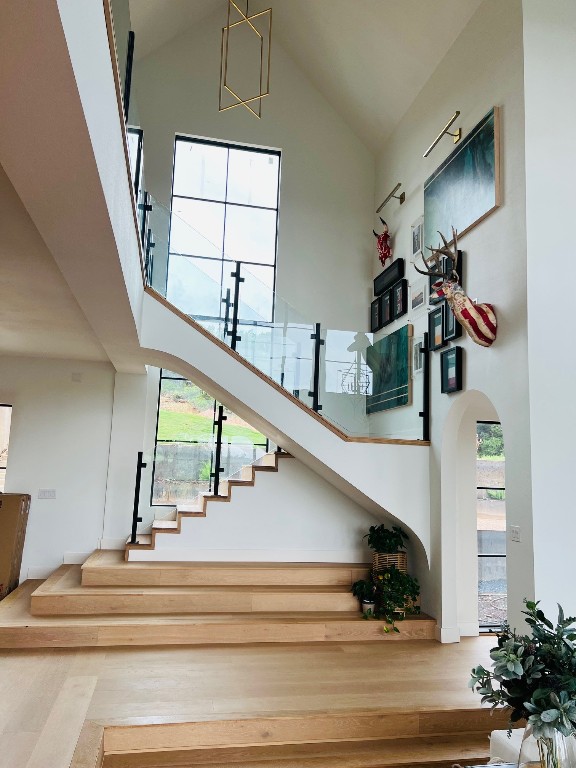 staircase with hardwood / wood-style flooring, a healthy amount of sunlight, and high vaulted ceiling